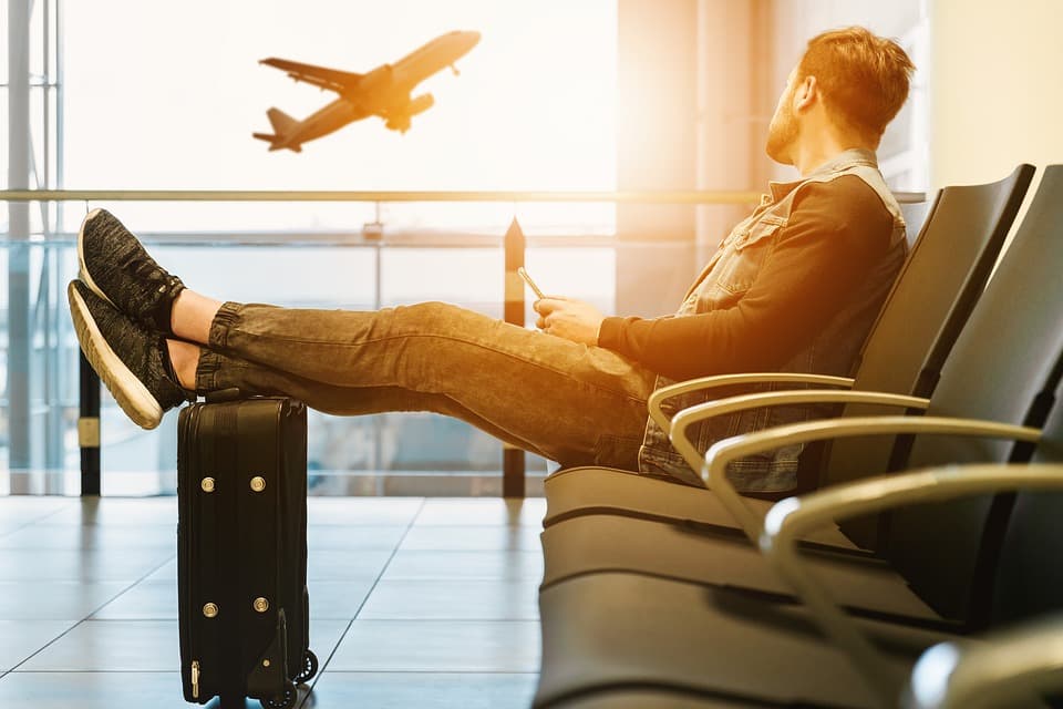 Passagier wartet mit Koffer am Gate, draußen startet ein Flugzeug